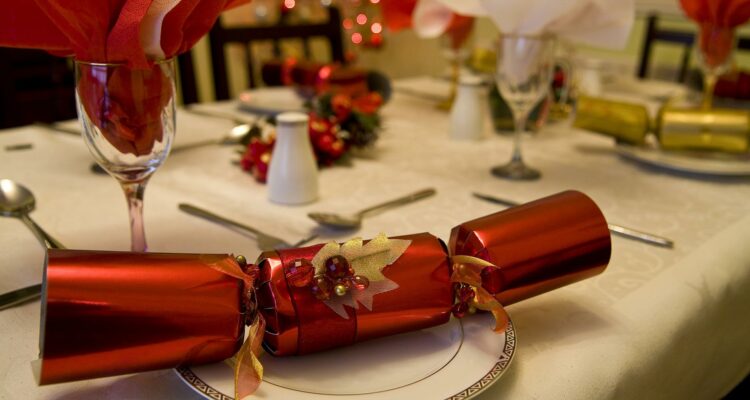 The image shows a red Christmas Cracker at the front of a table set out for Christmas Lunch